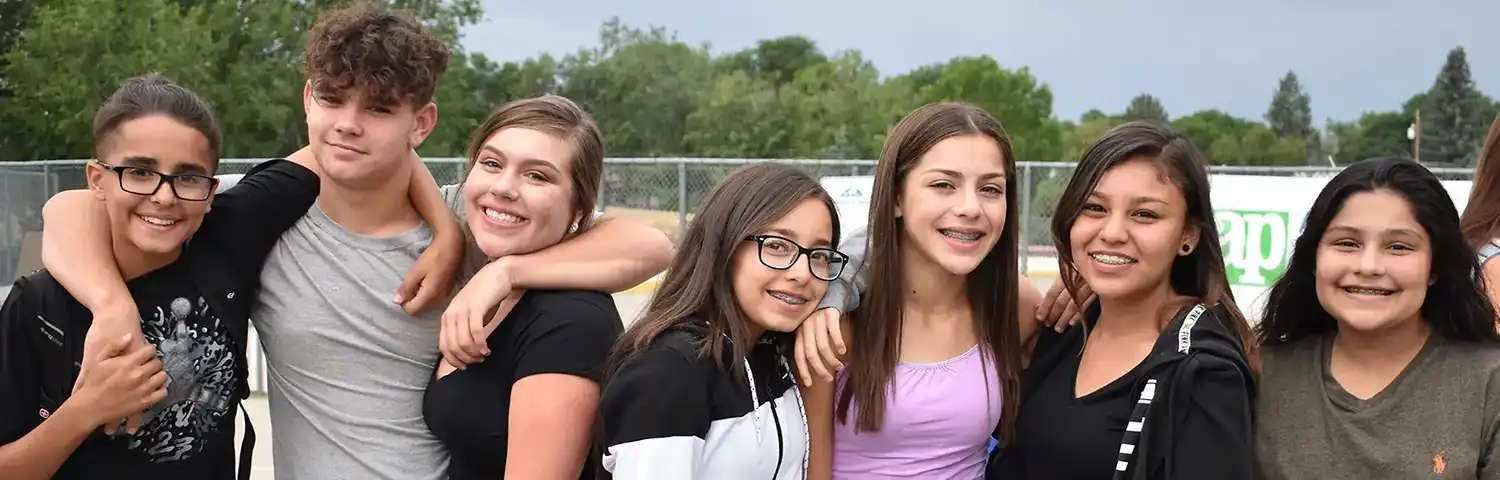 Smiling young people with arms around each other, standing outdoors.