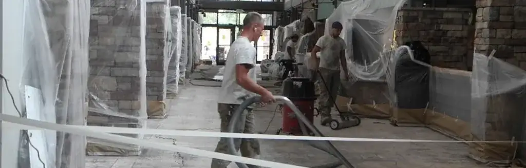 Two workers in a partially constructed space are cleaning amidst plastic sheetings.