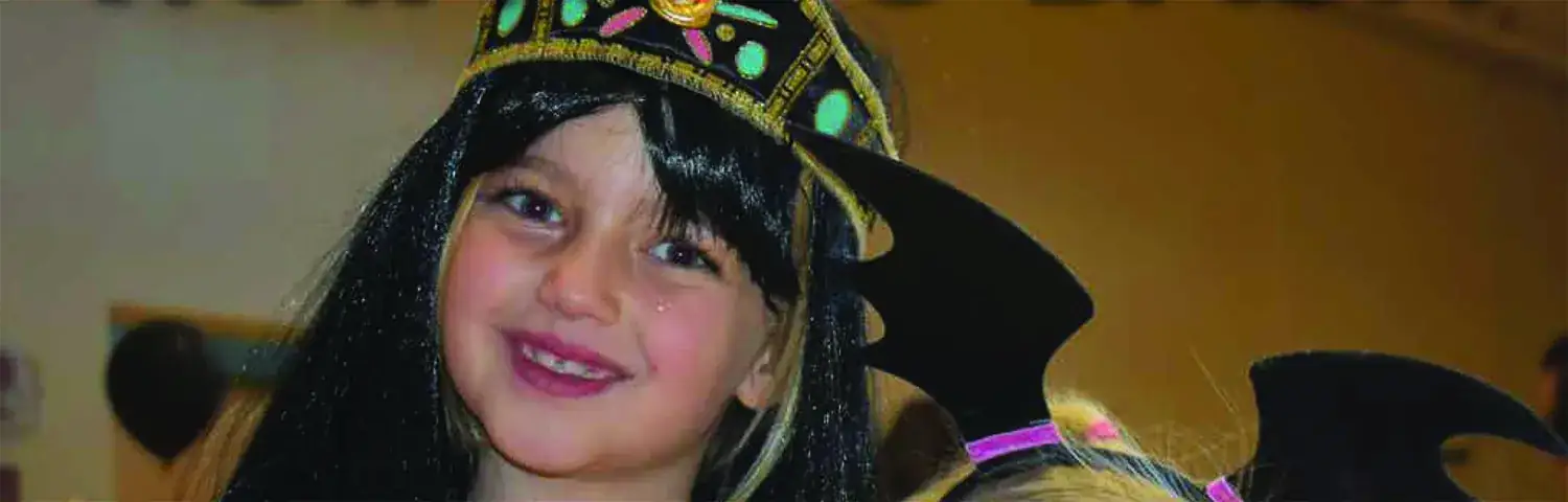 A young girl wearing a hat with a bat on it.