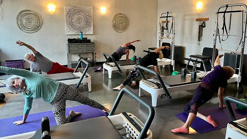 group of adults using Pilates reformer machines.