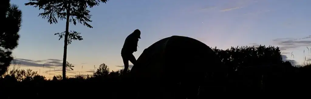 A silhouette of a person standing next to a tent.