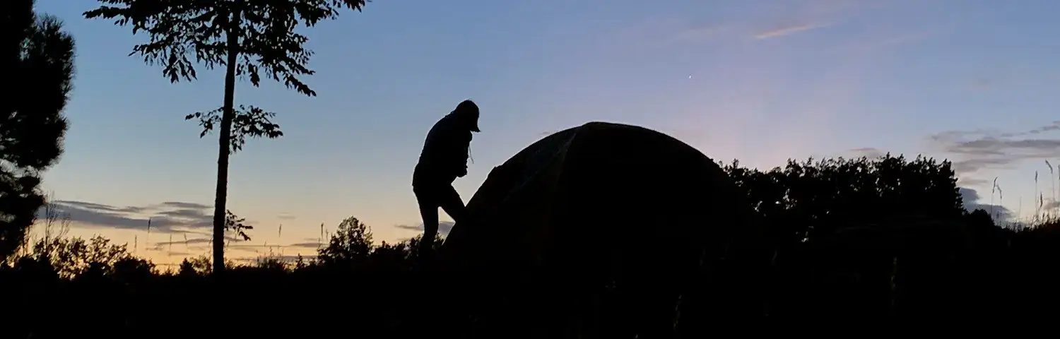 A silhouette of a person standing next to a tent.