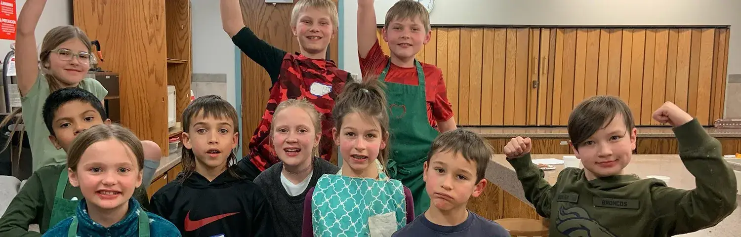 A group of children standing in a kitchen, wearing aprons.