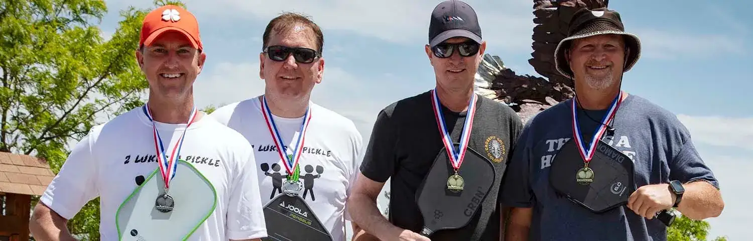 Four men wearing medals, holding pickleball paddles.