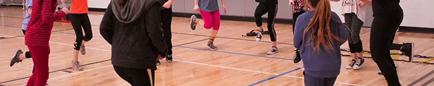A group of kids is having fun playing a game in a gymnasium under adult supervision.