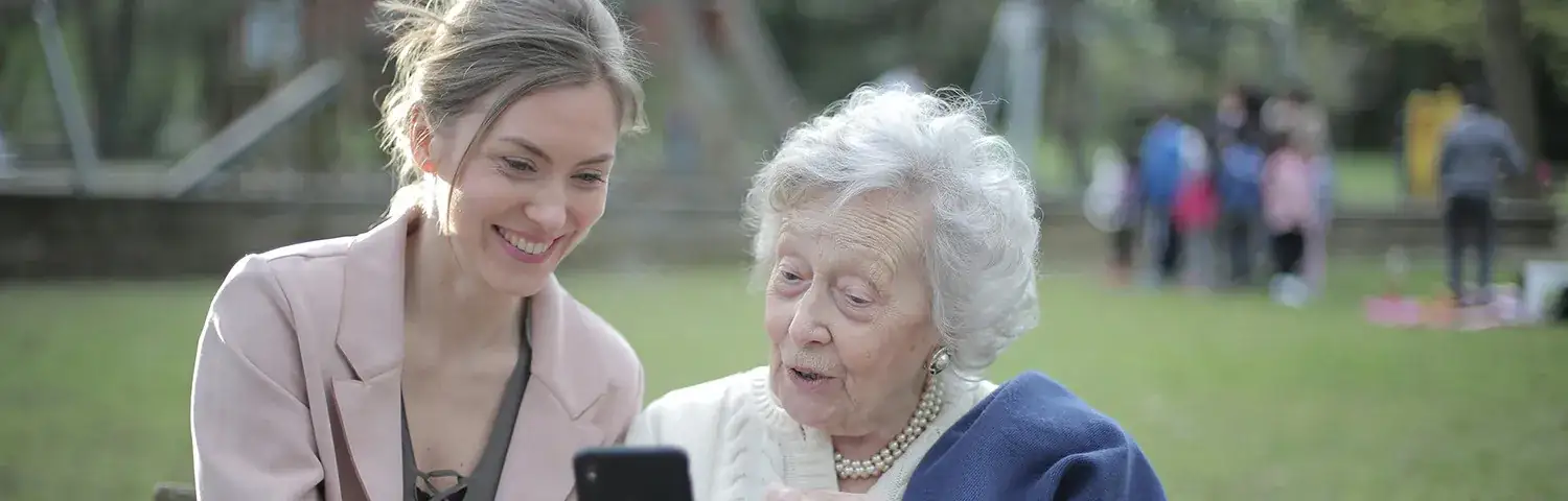A young woman and an elderly woman sit on a park bench.