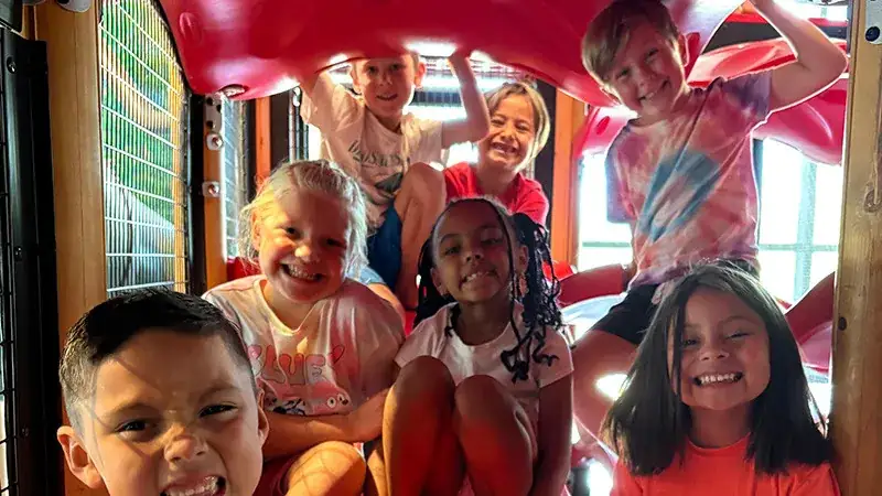 A group of children playing inside a colorful playground slide structure.