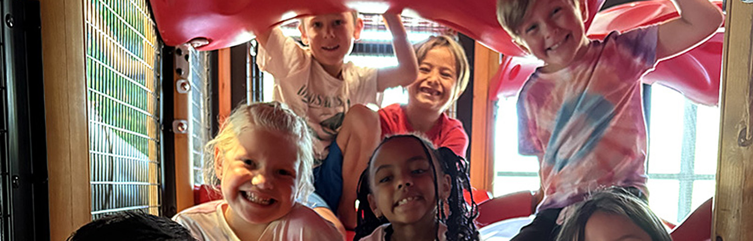 A group of children playing inside a colorful playground slide structure.
