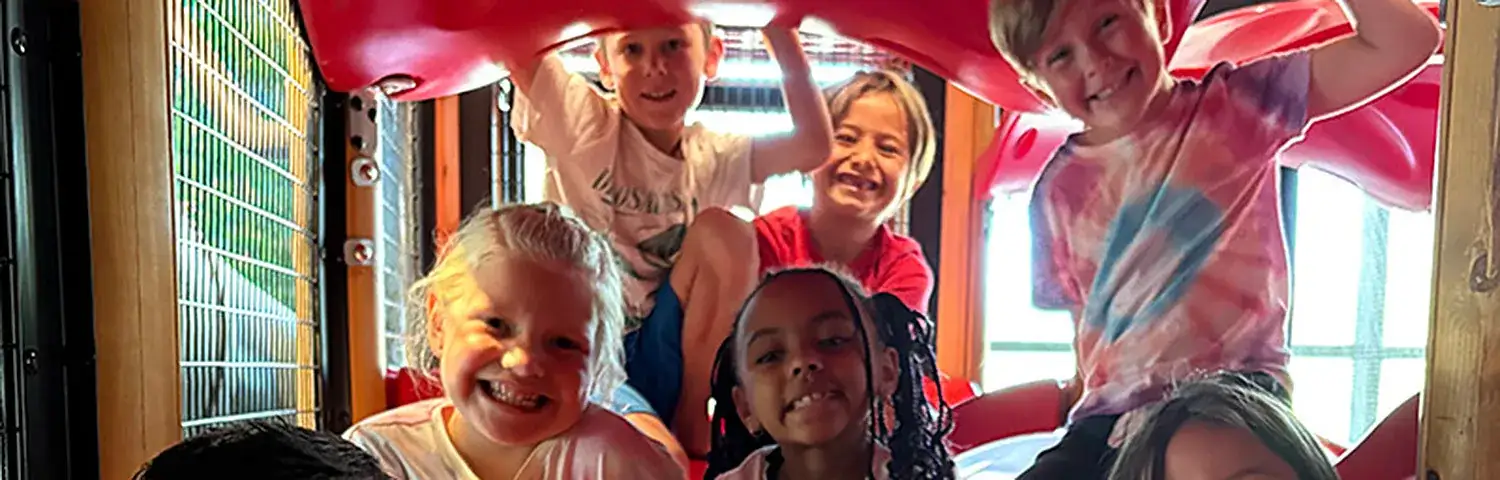 A group of children playing inside a colorful playground slide structure.
