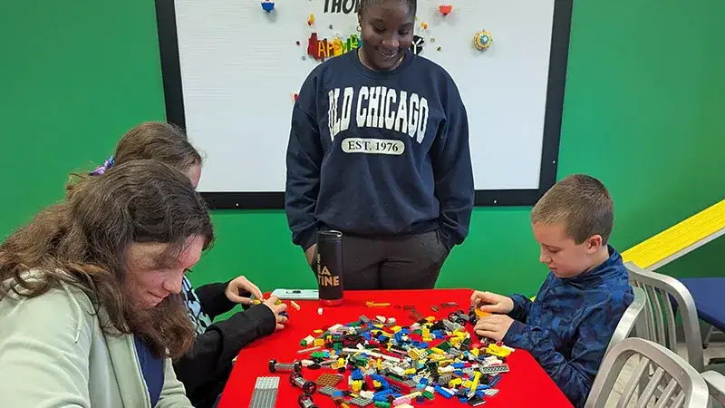 A small group gathers around a table filled with colorful LEGO pieces..