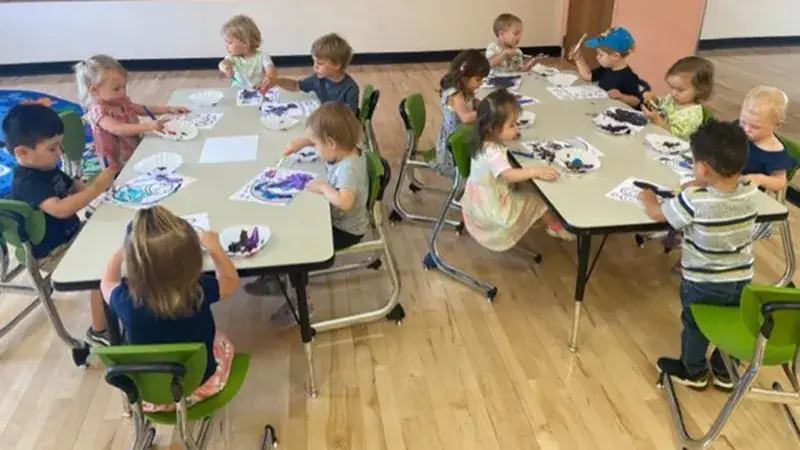 A group of young children engaged in a painting activity at tables.