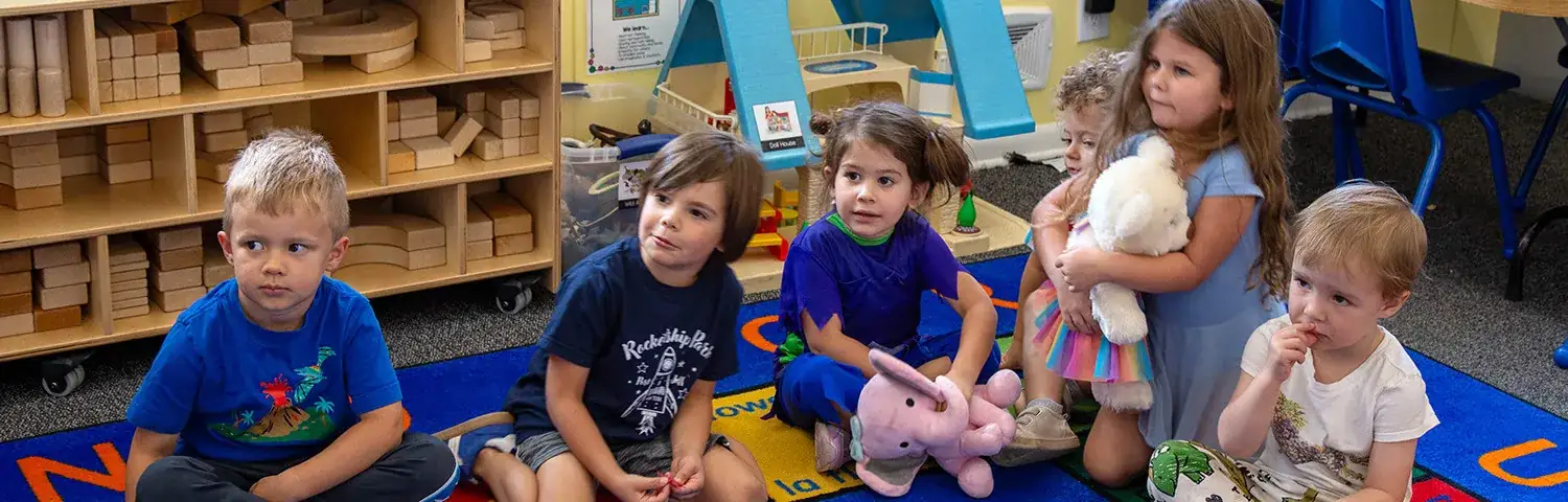 A group of children sits on a colorful carpet.