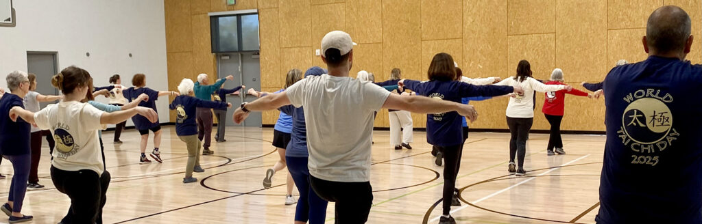 A group of people participates in a Tai Chi class in a gymnasium.