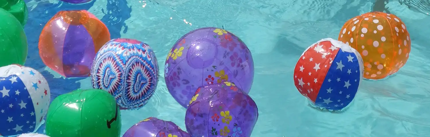 Beach Balls in a Pool banner Colorful patterned inflatable balls floating on water.