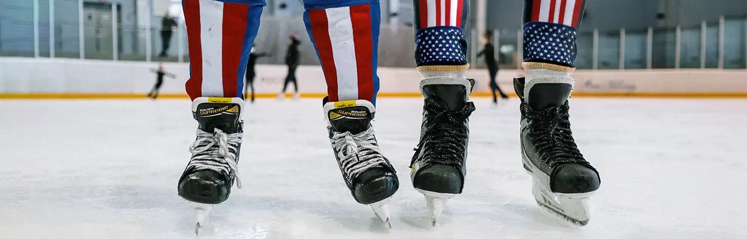 Close-up of two pairs of ice skates on an ice rink, with red, white and blue socks.