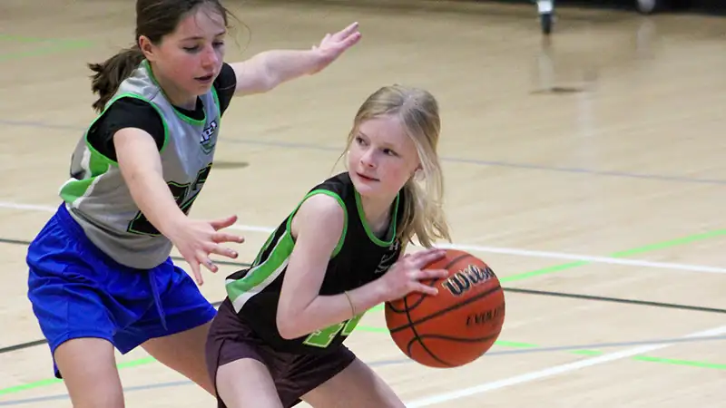 Youth basketball player holding the ball while another player defends during an indoor game.