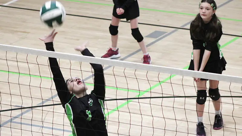 Youth volleyball player reaching up to set the ball near the net during an indoor game.