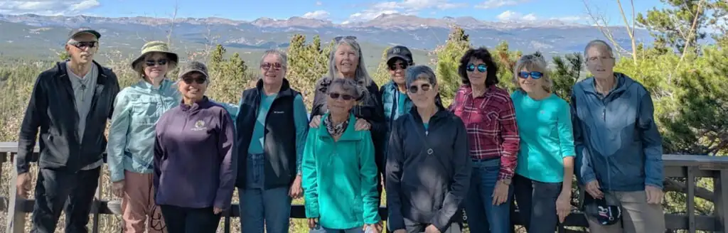 Group of adults posing outdoors with a forest and mountain landscape in the background.