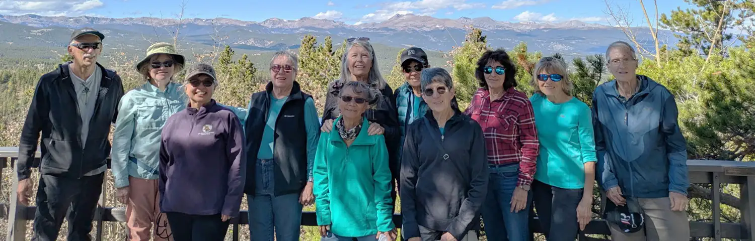 Group of adults posing outdoors with a forest and mountain landscape in the background.