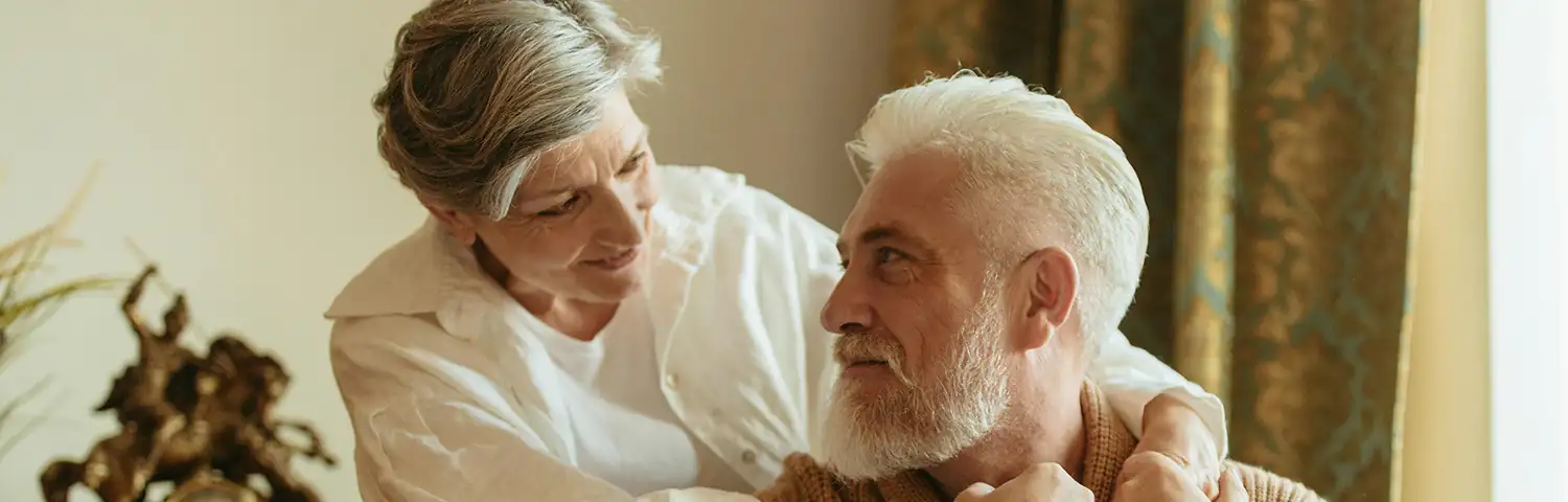 Older woman and man embracing as they look into each other’s eyes with smiles.