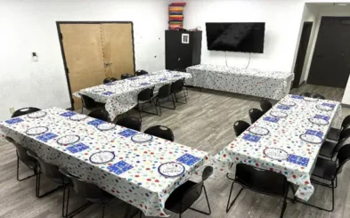 Room set up with three tables covered in colorful party-themed tablecloths, each with plates and napkins arranged, and a wall-mounted TV.