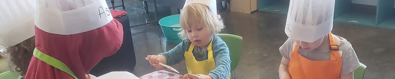 Children in chef hats are gathered around a table, engaged in a cooking activity.