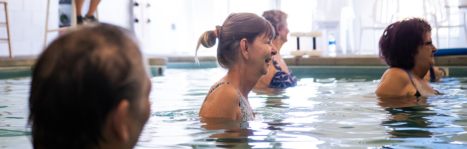 Group of older adults smiling and standing in indoor pool during water exercise class.
