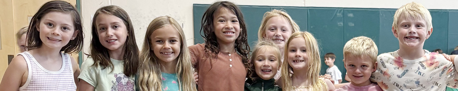 Nine smiling elementary-age children pose together in a school gymnasium.